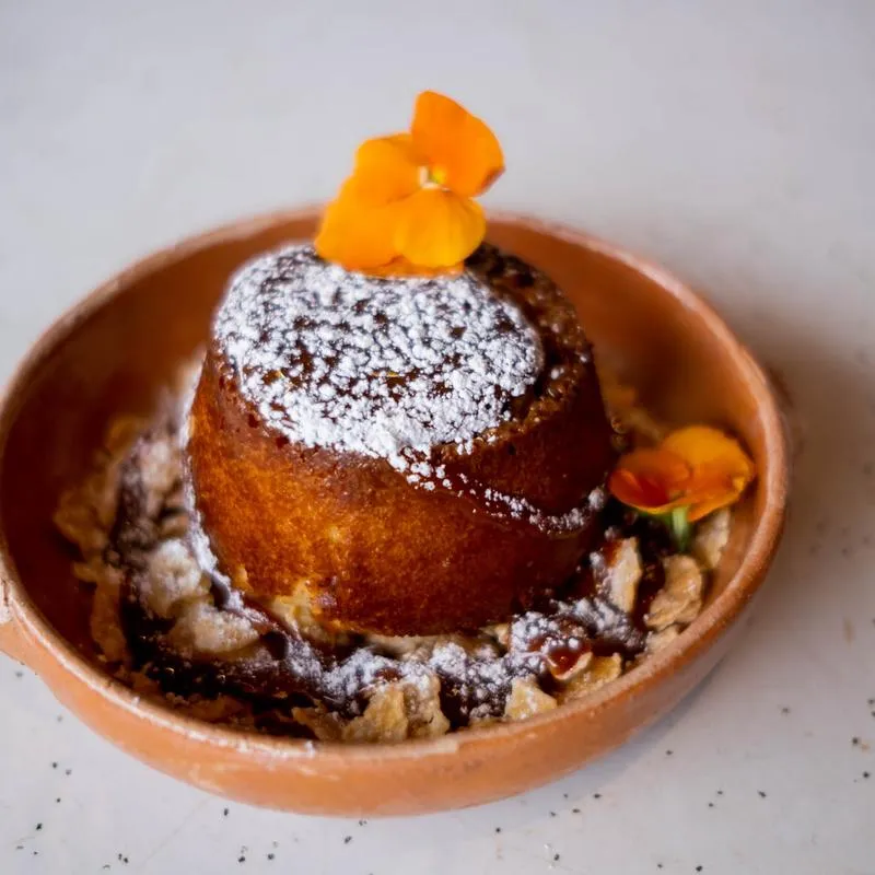 A golden baked pastry served in a clay dish and dusted with sugar