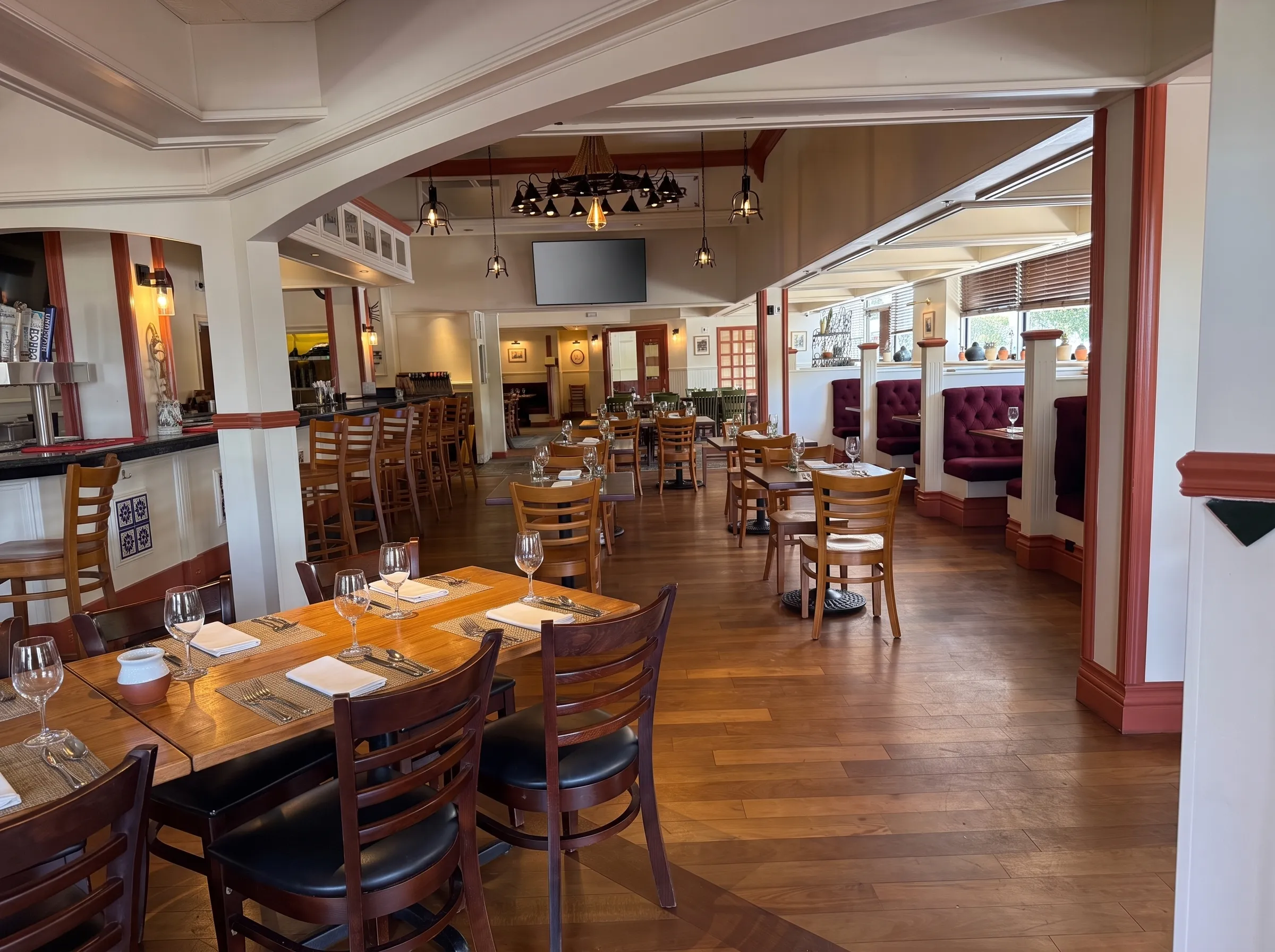 The main dining room at Panfila: burgundy tufted booths, olive-green chairs, farm tables and a wrought-iron chandelier