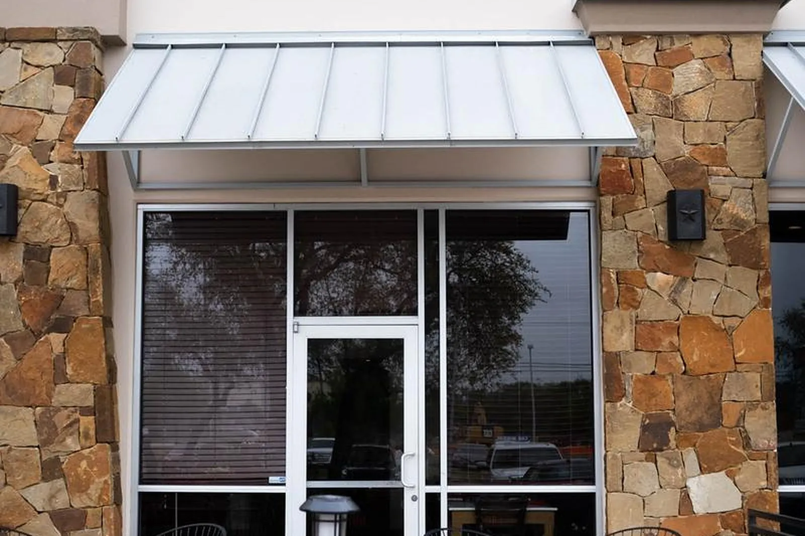The Panfila entrance at The Shops at Fossil Creek: stone columns, a metal awning and the patio tables