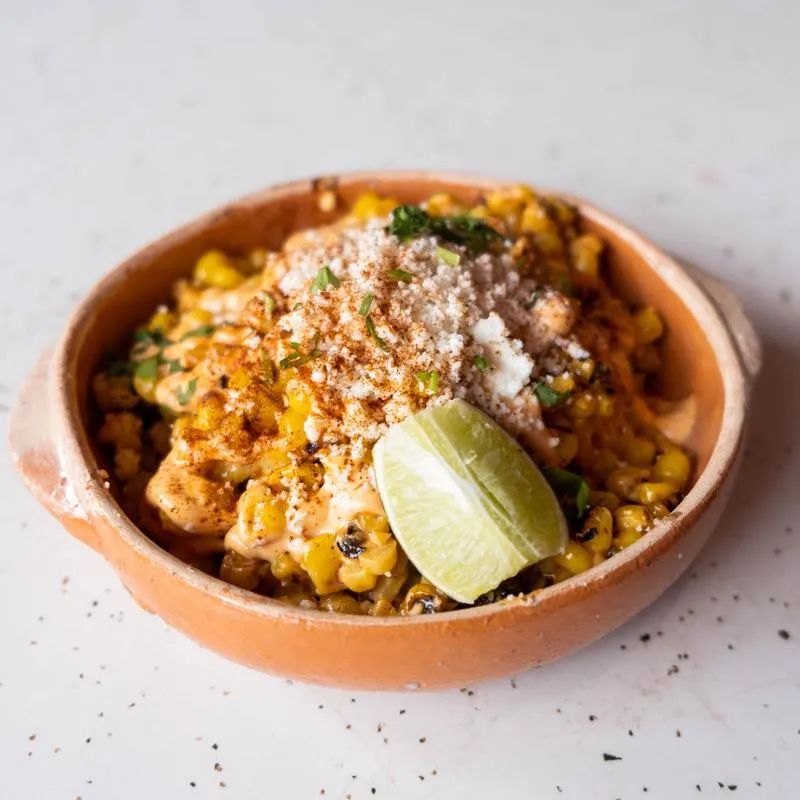 Mexican street corn in a terracotta cazuela with lime and queso fresco