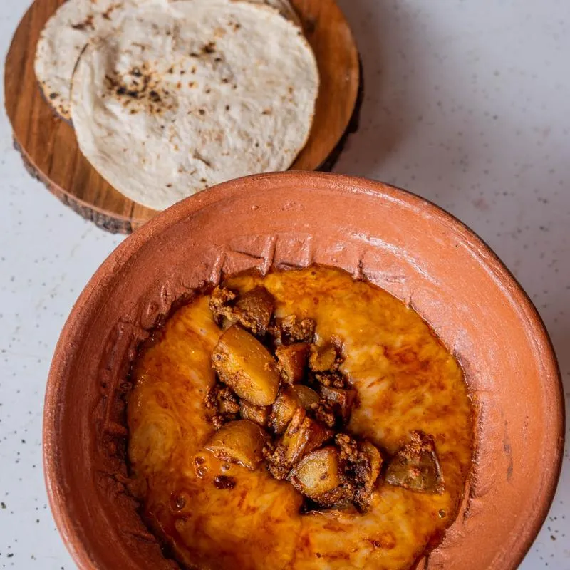 Queso fundido with chorizo in a clay dish beside a basket of warm tortillas