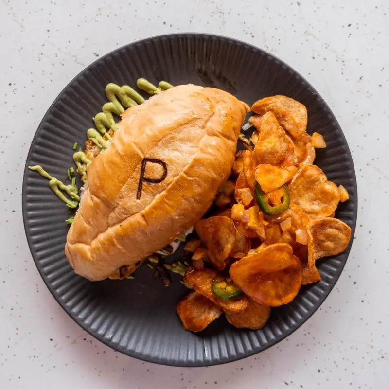 A torta on a house bolillo stamped with a P, served on a black plate with chips