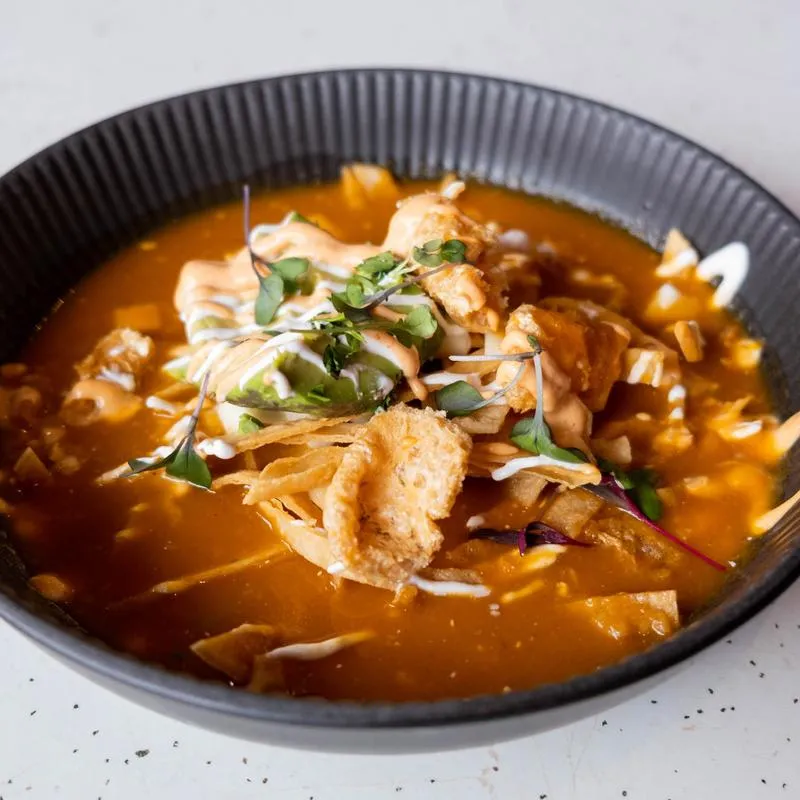 Tortilla soup topped with crisp tortilla strips, crema and avocado